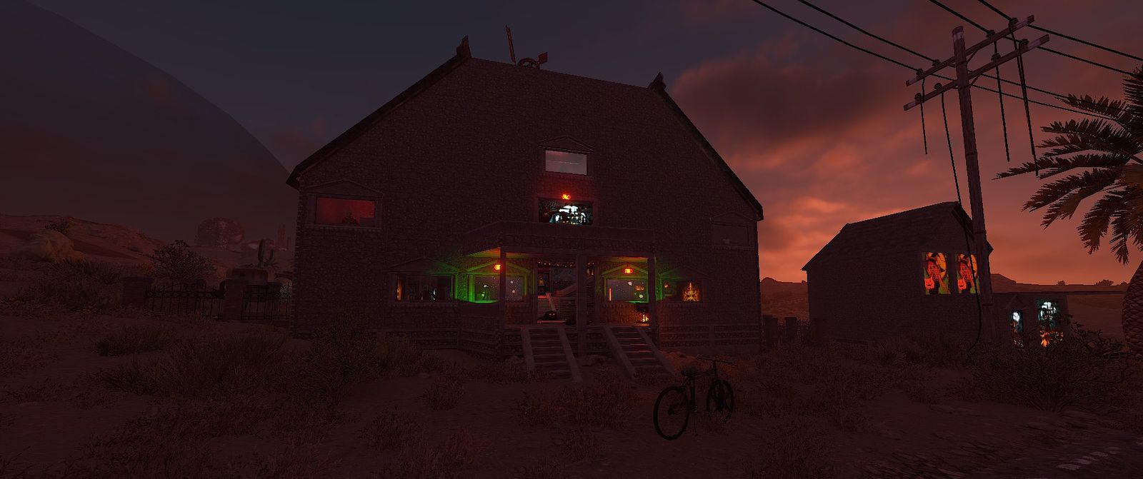 A player-built haunted mansion at dusk, its windows glowing orange and green, with a smaller haunted shed beside it